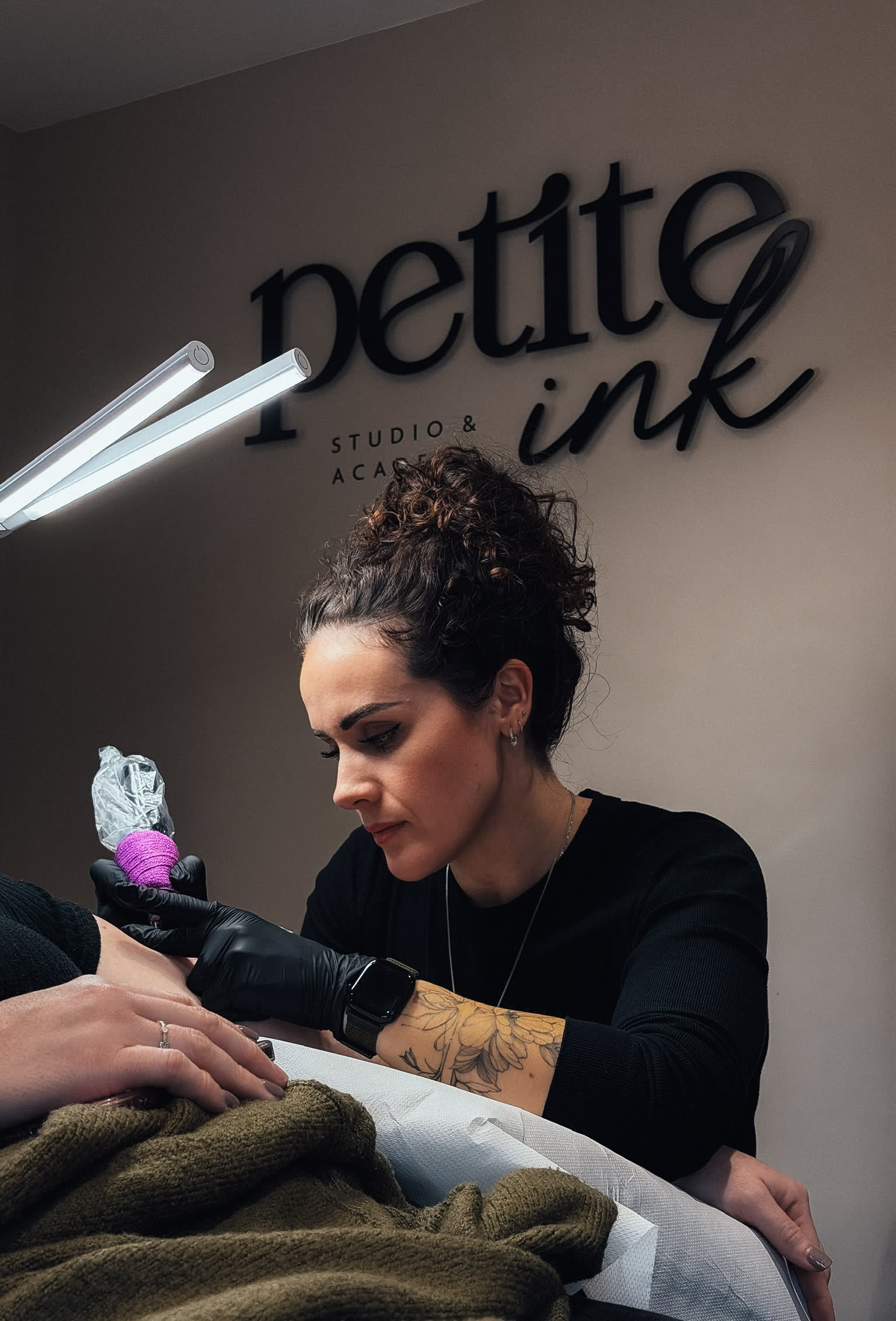 Kayleigh tattooing beneath the Petite Ink studio sign