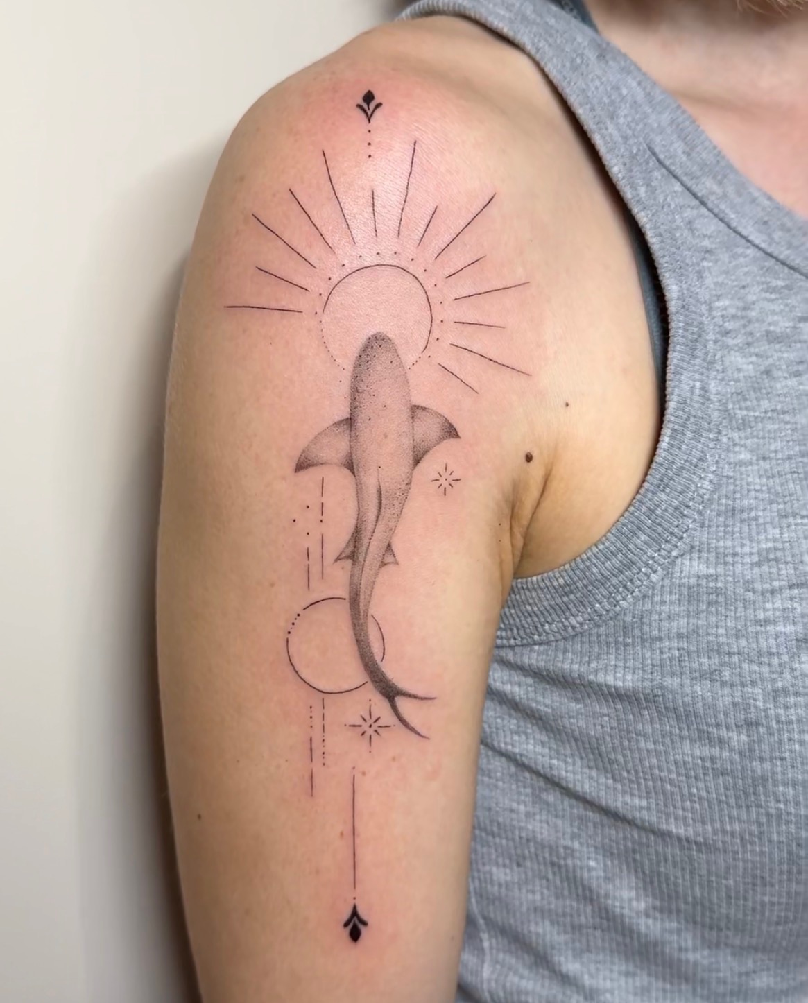 A fine line shark beneath a sunburst on the upper arm